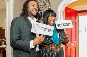 Enthusiastic man and woman holding "C-STEM" and "Verizon" signs, promoting STEM education and Verizon's involvement.